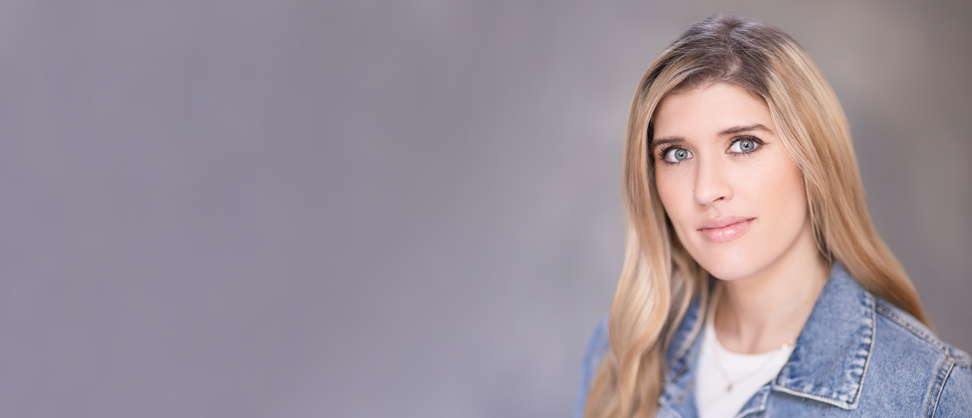 Blonde lady smiling softly with a grey backdrop